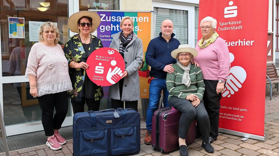 Das Foto zeigt eine Gruppe Menschen mit Koffern und WirWunder-Werbung.