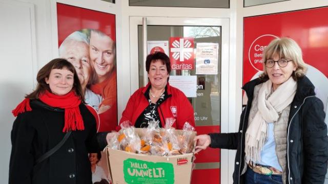Tabea Below (l.) und Daniela Ramb (r.) aus der khg übergeben die gepackten Plätzchentüten vor der Sozialstation an Christiane Koch von der Caritas. | Foto: Caritas