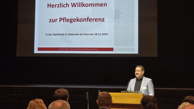 Das Foto zeigt einen Mann am Stehpult vor einer großen Leinwand mit dem Konferenztitel.