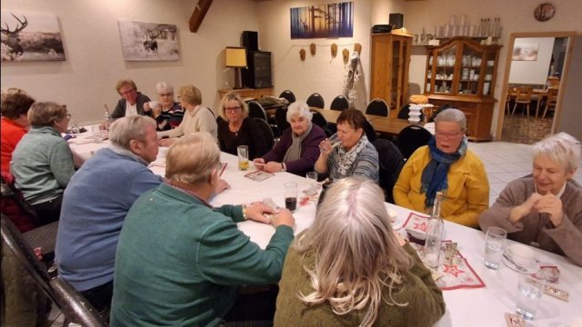 Das Foto zeigt einen Gastraum mit einem langen Tisch, an dem Menschen sitzen und miteinander erzählen.